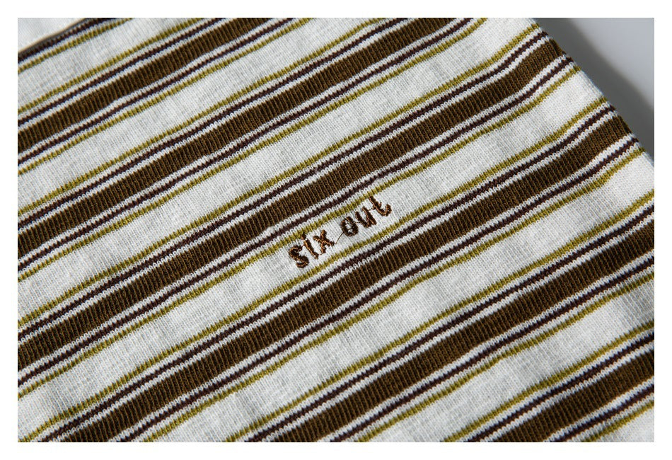 Close-up of small brown embroidered lettering on the cream, brown, and olive striped fabric.