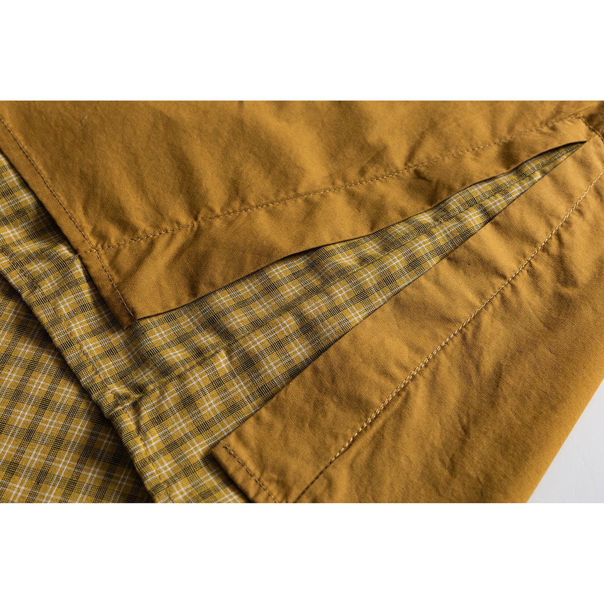 Close-up of a mustard shirt's hem, showing the yellow plaid lining and stitched panels.