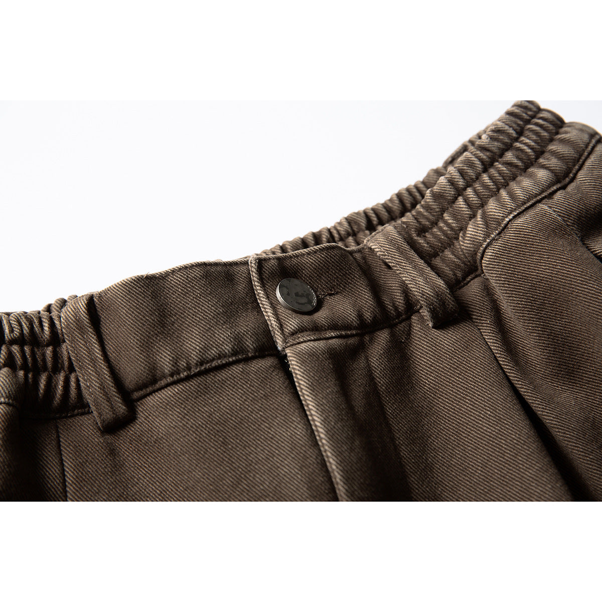 Close-up of brown trousers showing the elastic waistband, belt loops, and button closure.