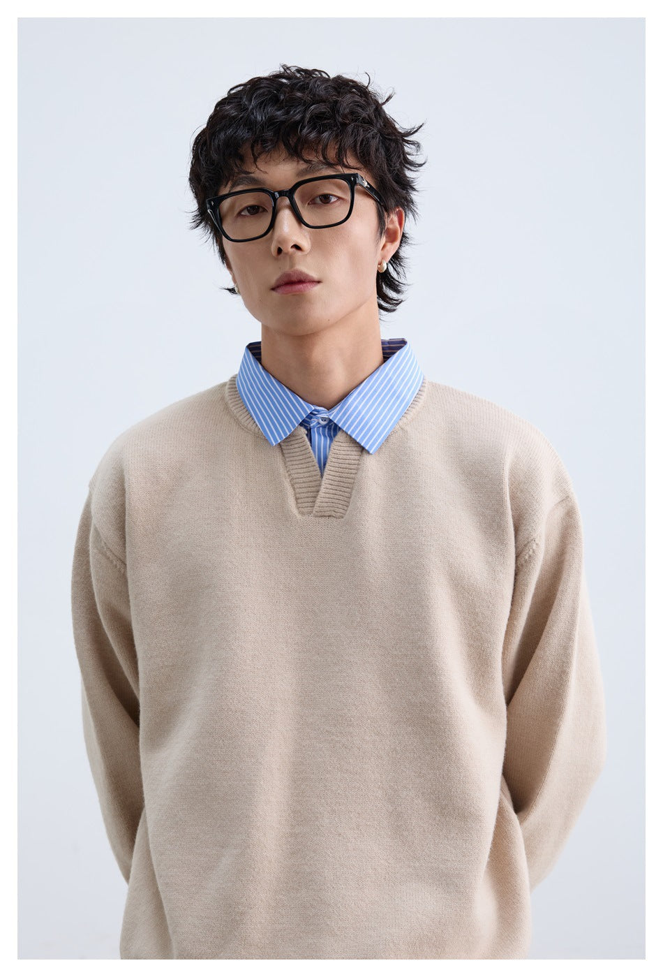 Close-up of a beige sweater's knit texture and V-neck layered over a blue striped shirt.