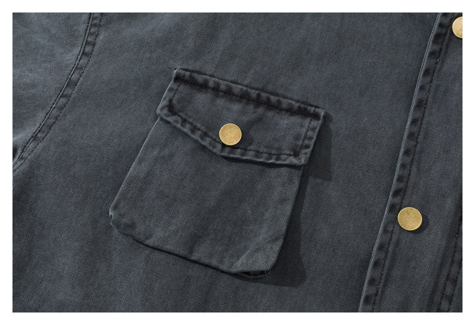 Close-up of a charcoal jacket's large flap pocket with a brass snap and matching brass front snaps.