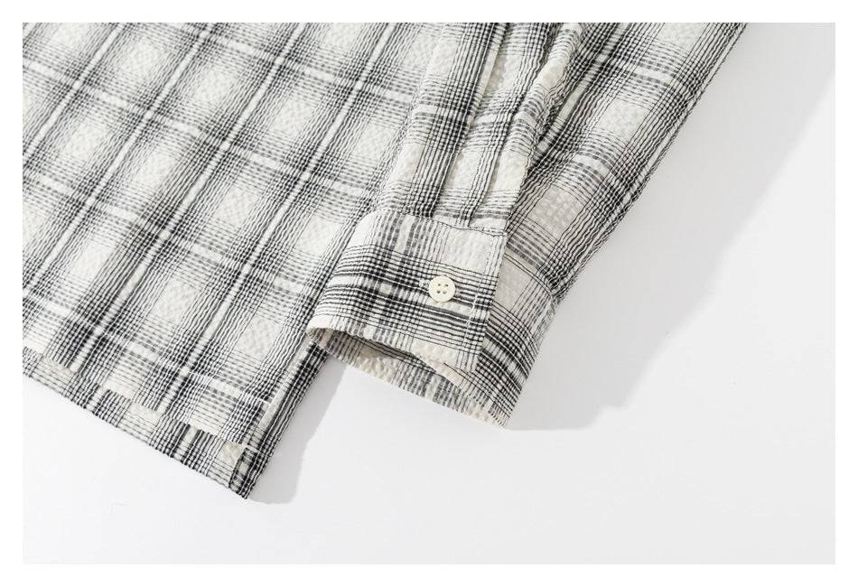 Close-up of the buttoned cuff and hem of a cream and black plaid shirt laid flat.