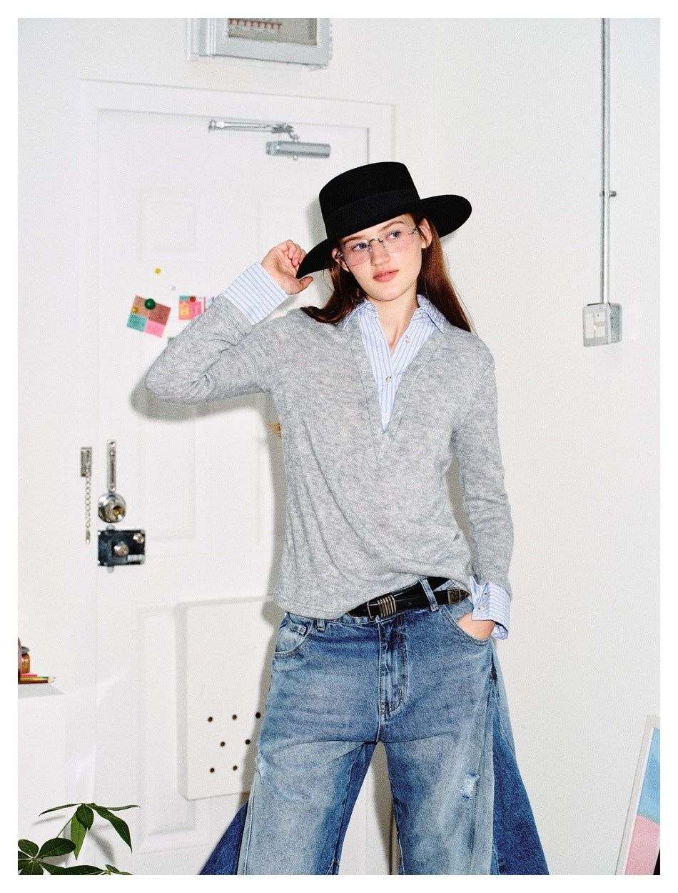 Model in gray V-neck top with striped shirt collar and cuffs, black hat, belt and blue jeans, hand in pocket