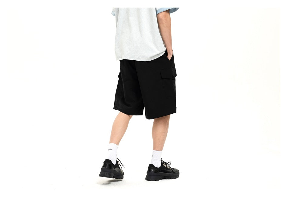 Rear three-quarter view of a model wearing black cargo shorts with flap side pockets.