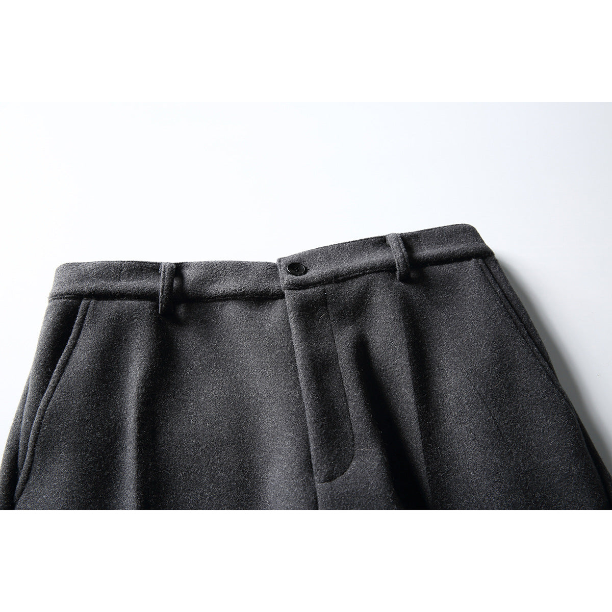 Close-up of charcoal trousers’ front waistband, belt loops, button, fly and slanted pockets.