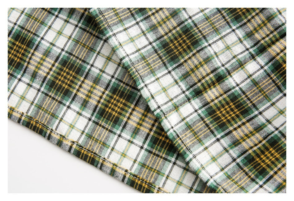 Close-up of the stitched hem and plaid pattern on a white, green, black, and mustard shirt.