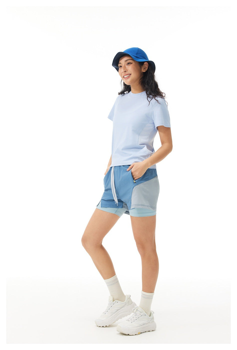 Woman wearing a pale blue short-sleeve shirt and blue-gray color-block shorts, shown from the front.