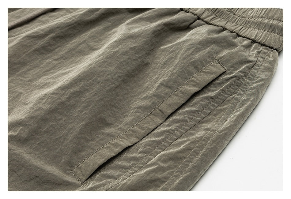 Close-up of an angled side pocket and stitched seams on olive-gray shorts.