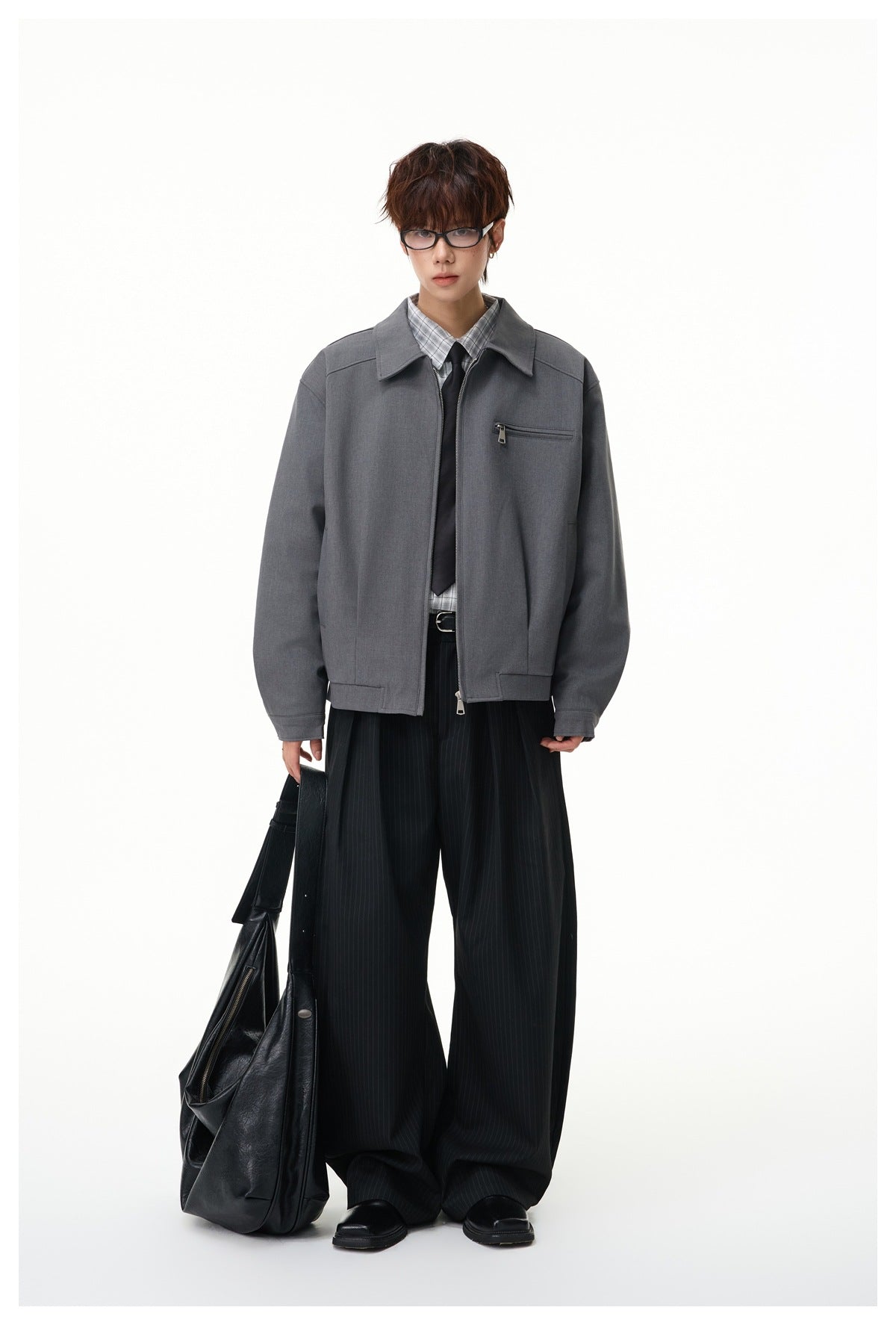 Model wearing a charcoal gray zip-front jacket with a pointed collar and chest zip pocket, styled with black trousers.