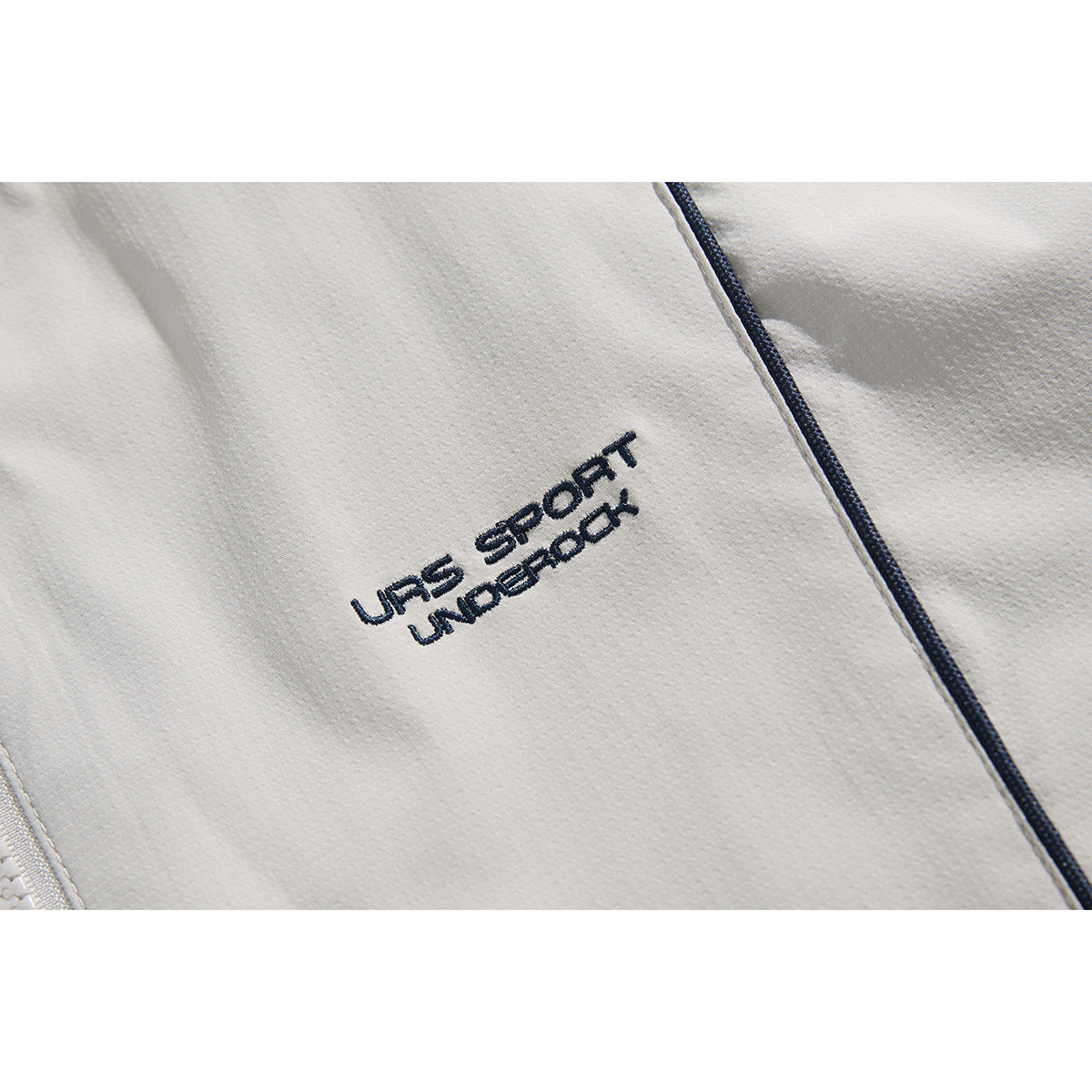 Close-up of embroidered dark lettering and contrast piping on a light gray jacket.