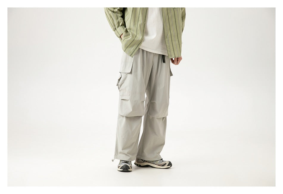 Side view of a model wearing light gray loose cargo pants with large flap pockets and drawstring hems.