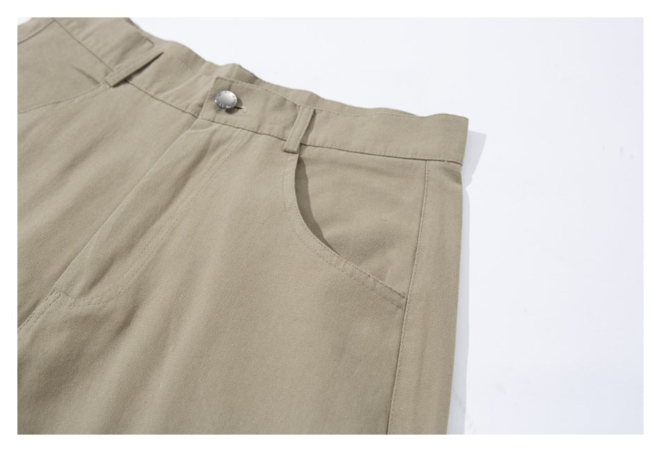 Angled close-up of beige trousers showing the buttoned waistband, belt loop, and curved front pocket.