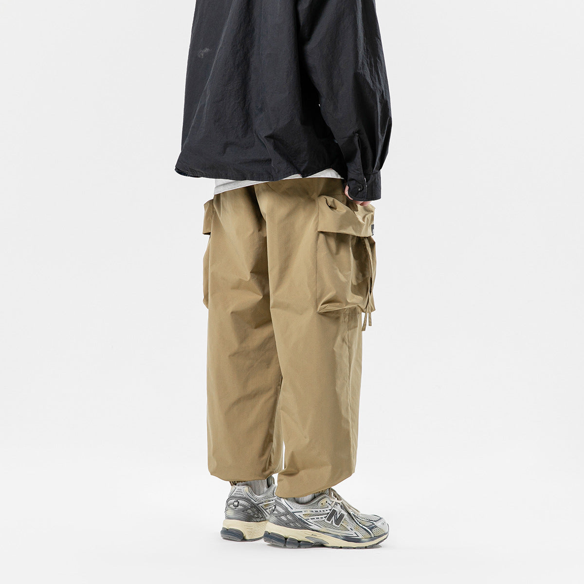 Rear view of a model wearing loose tan cargo pants with large flap pockets.