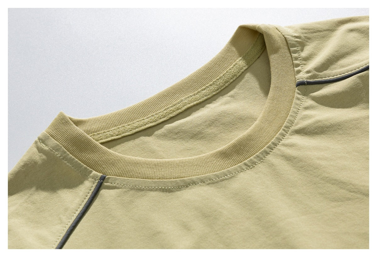 Close-up of a pale olive T-shirt's ribbed crew neckline and dark contrast piping at the shoulder.
