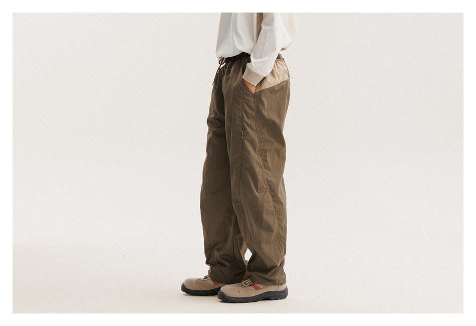 Side view of a model wearing loose olive-brown pants with a side pocket and gathered cuffs.