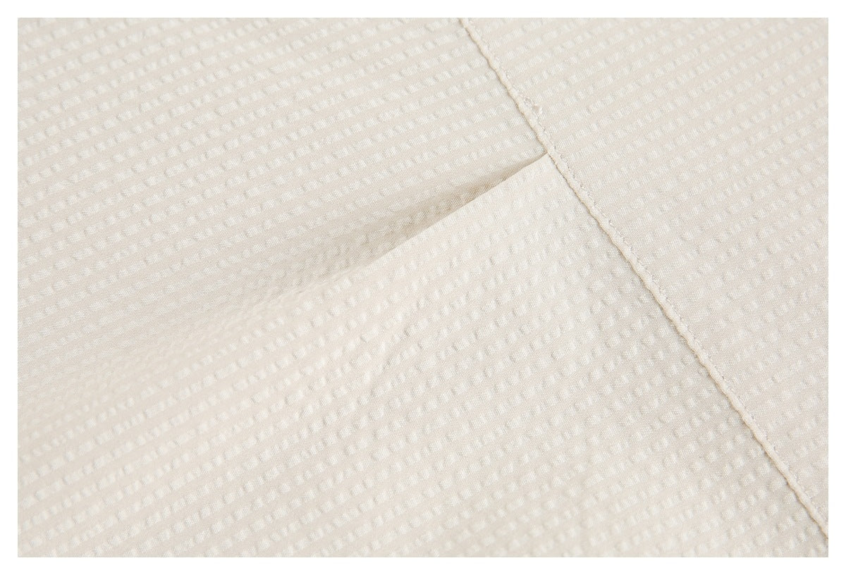 Close-up of ivory fabric with a subtle raised texture and a diagonal stitched seam.
