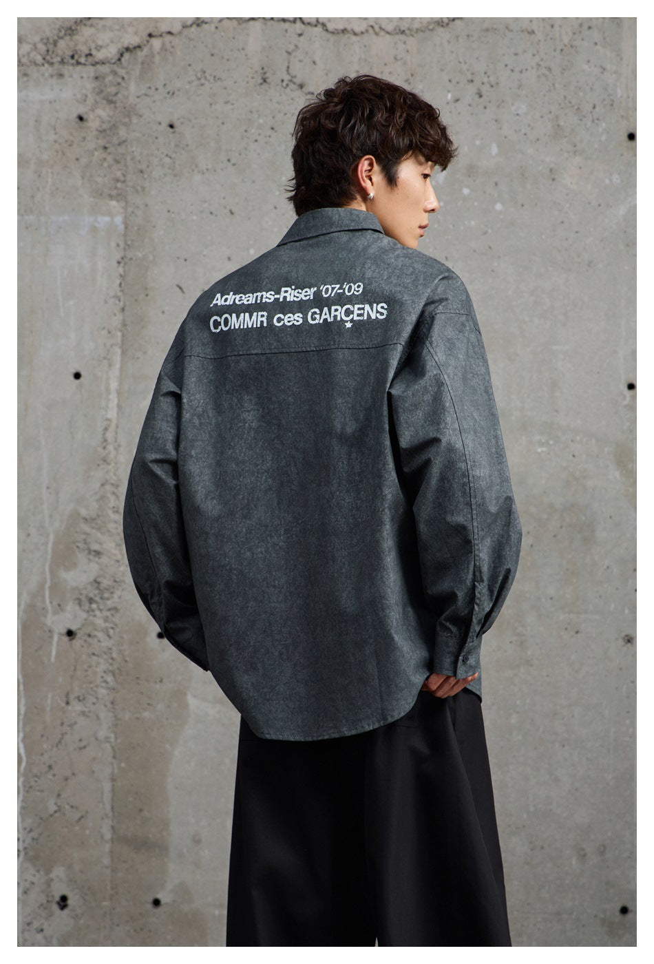 Back view of a model wearing a charcoal button-up shirt with large white lettering across the upper back.