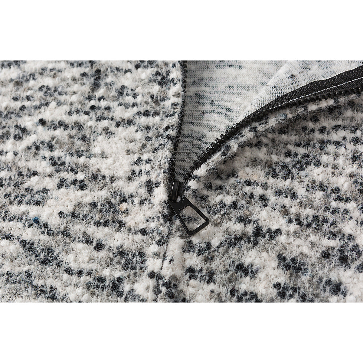 Close-up of a black zipper and pull on textured black-and-white jacket fabric.