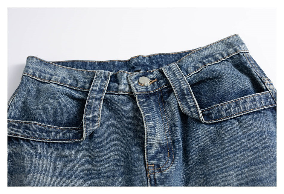 Cropped front view of blue distressed jeans showing the waistband, button closure and oversized angular pockets.