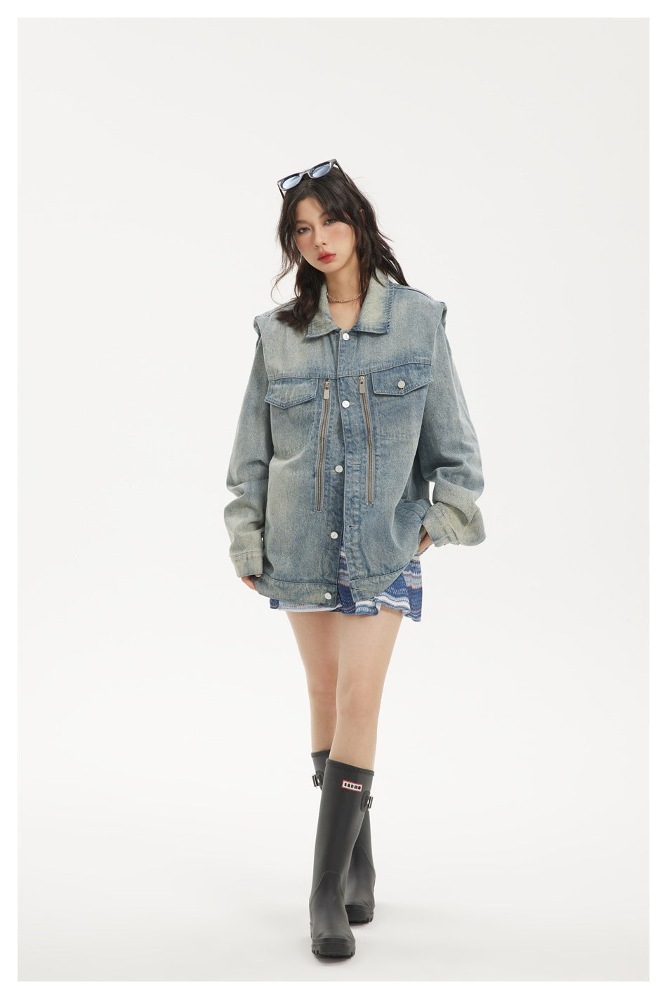 Full-length model wearing an oversized light-wash denim jacket with snap buttons, flap pockets and vertical zippers.