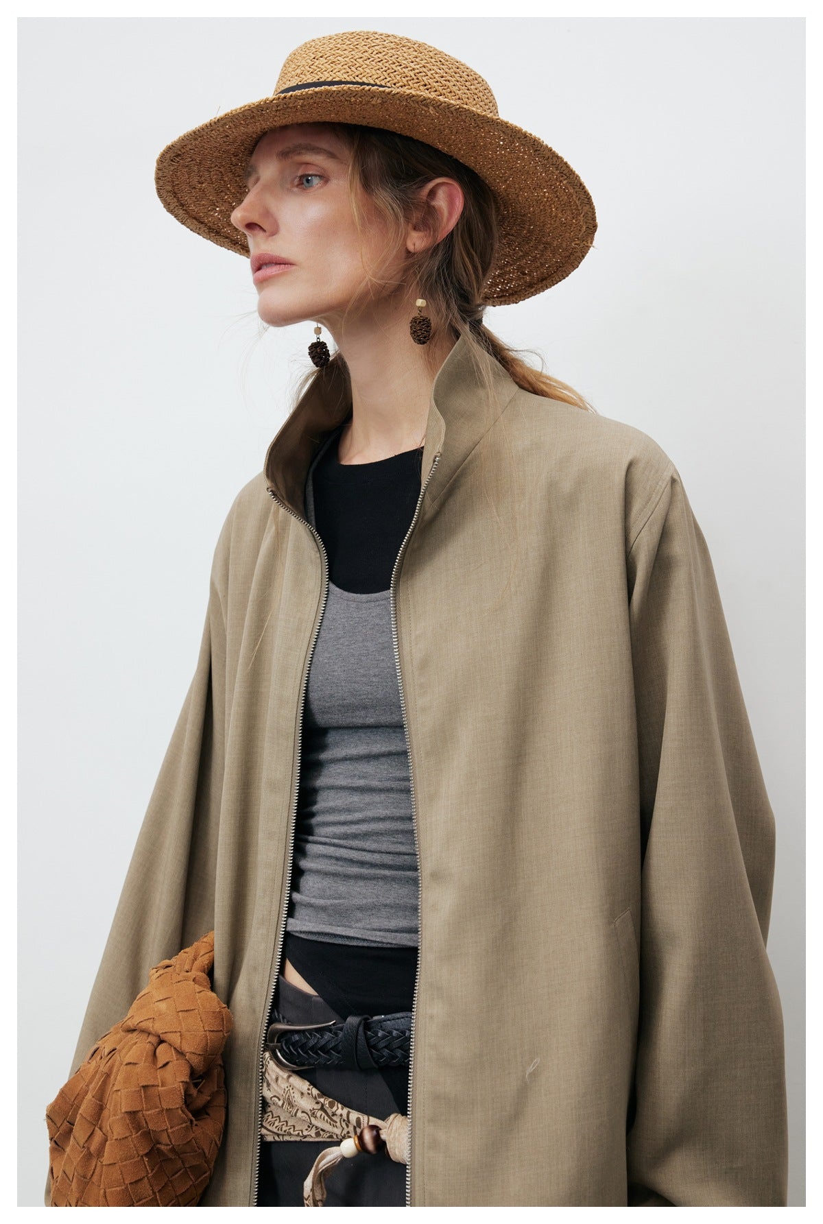 Close view of a model wearing an open taupe jacket with a stand collar and front zipper.
