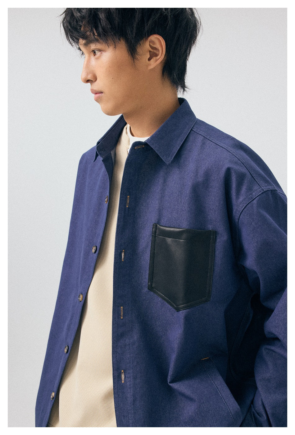 Close view of a model wearing a blue overshirt, highlighting its black chest pocket and button front.