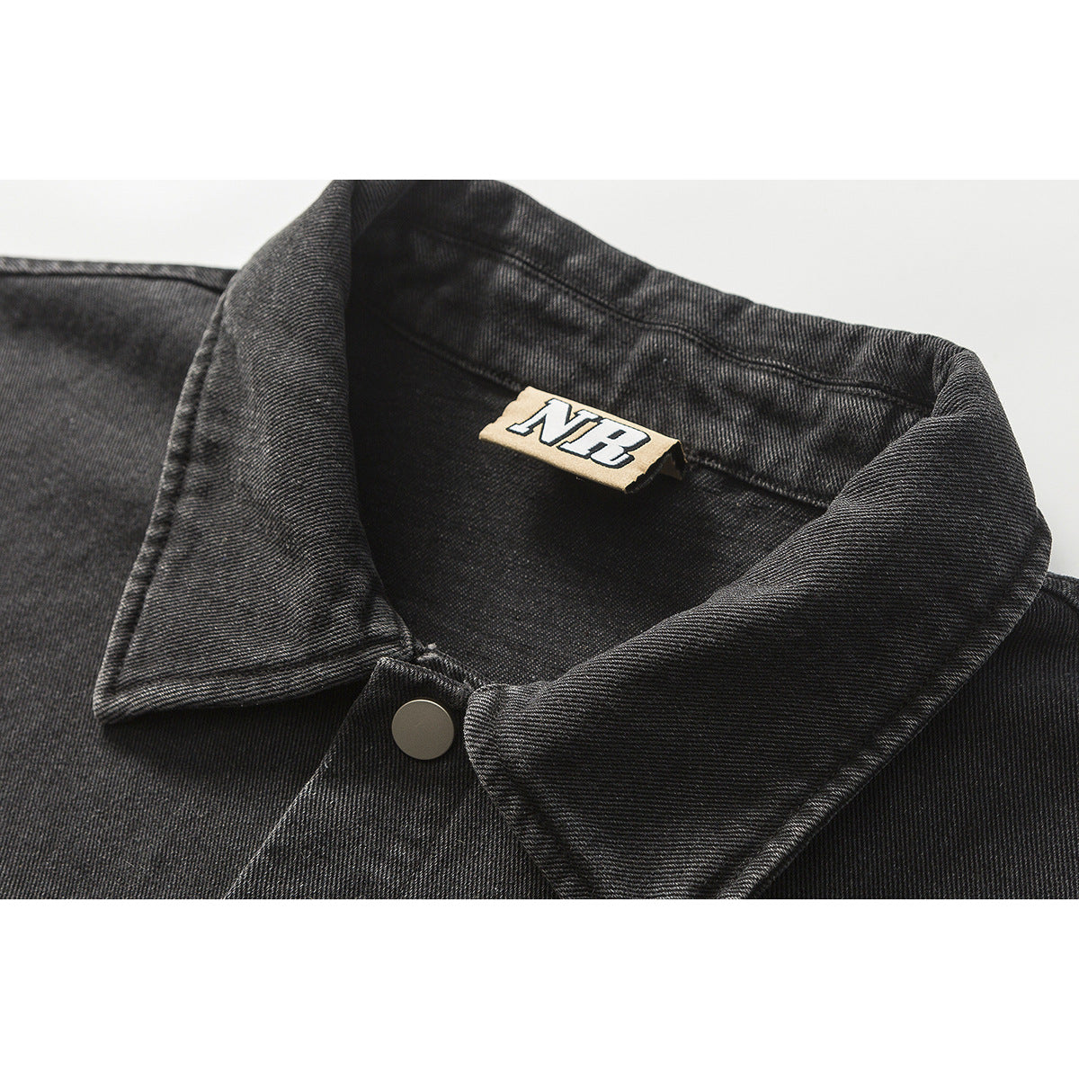 Close-up of a black denim jacket collar, silver snap, and small NB neck label.