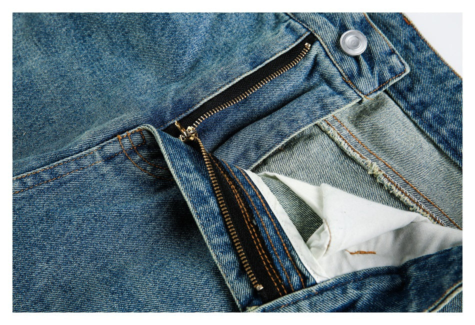 Close-up of blue washed jeans with the fly open, revealing a metal zipper and white pocket lining.