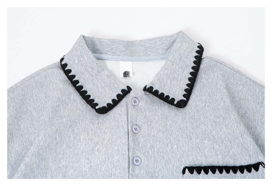 Close-up of a heather gray polo shirt with a black scalloped-trim collar, pale buttons and matching pocket trim.