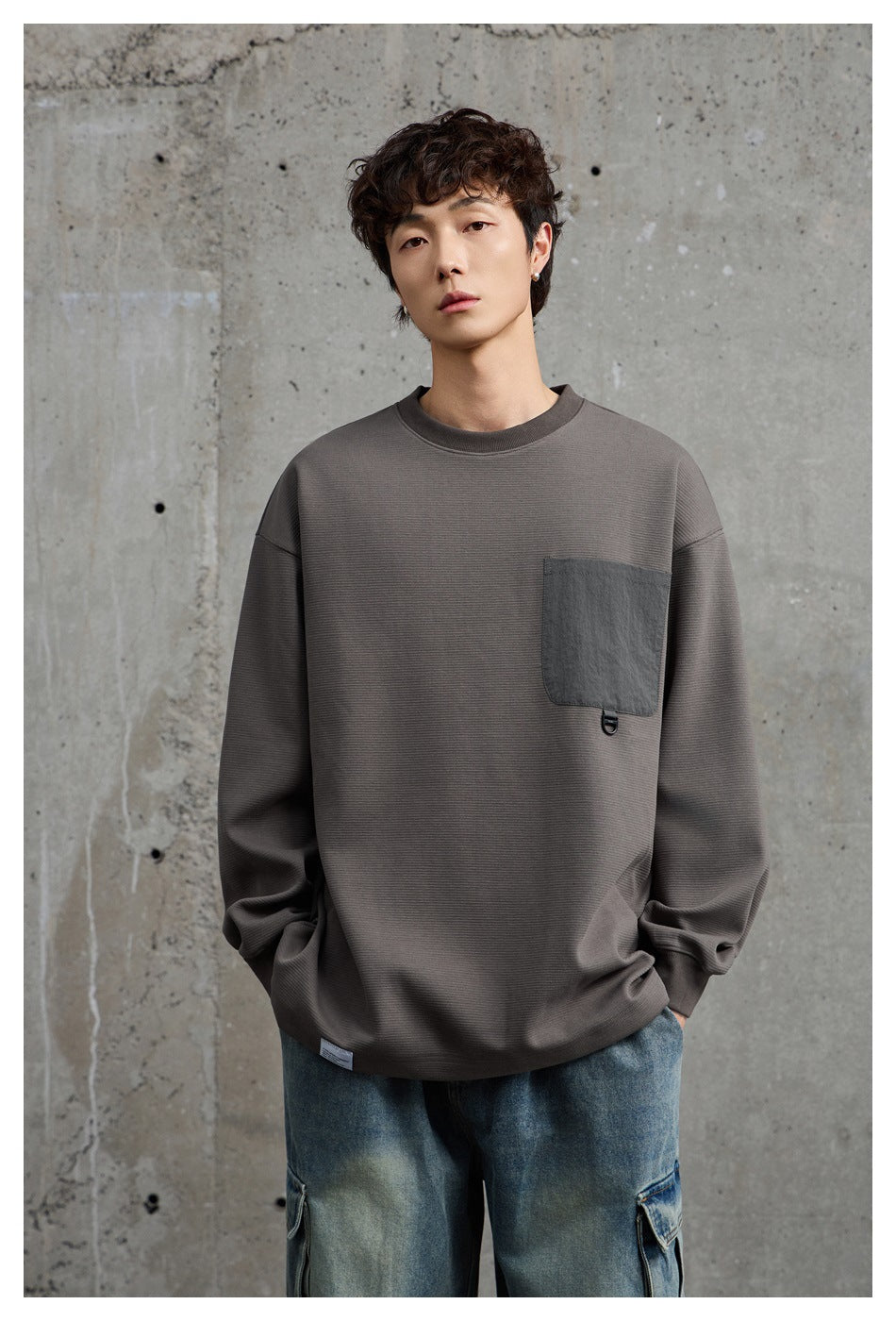 Front view of a model wearing a charcoal gray oversized sweatshirt with a dark chest pocket.