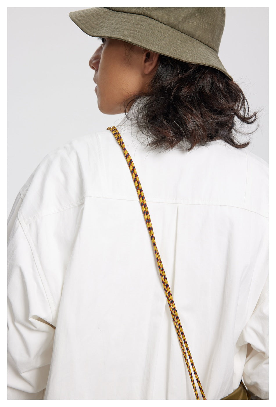 Close rear view of a model wearing a loose white shirt with a back yoke and a colorful cord crossing the shoulder.
