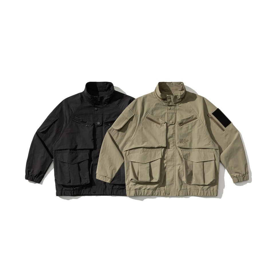 Two utility jackets shown side by side: one black and one khaki, both with high collars and multiple pockets.