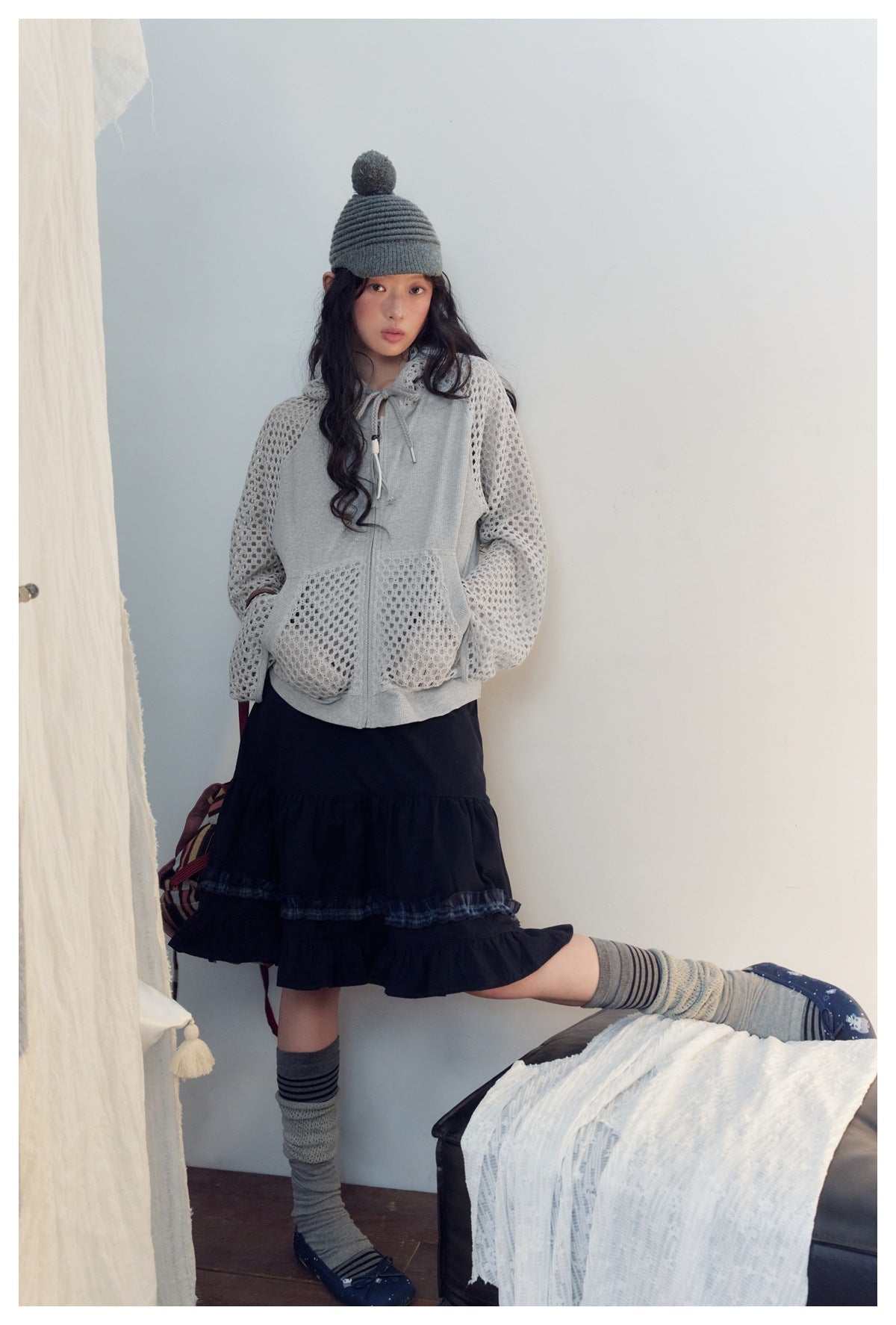 Model wearing a light gray zip hoodie with open-knit mesh sleeves and pockets, shown with a black ruffled skirt.