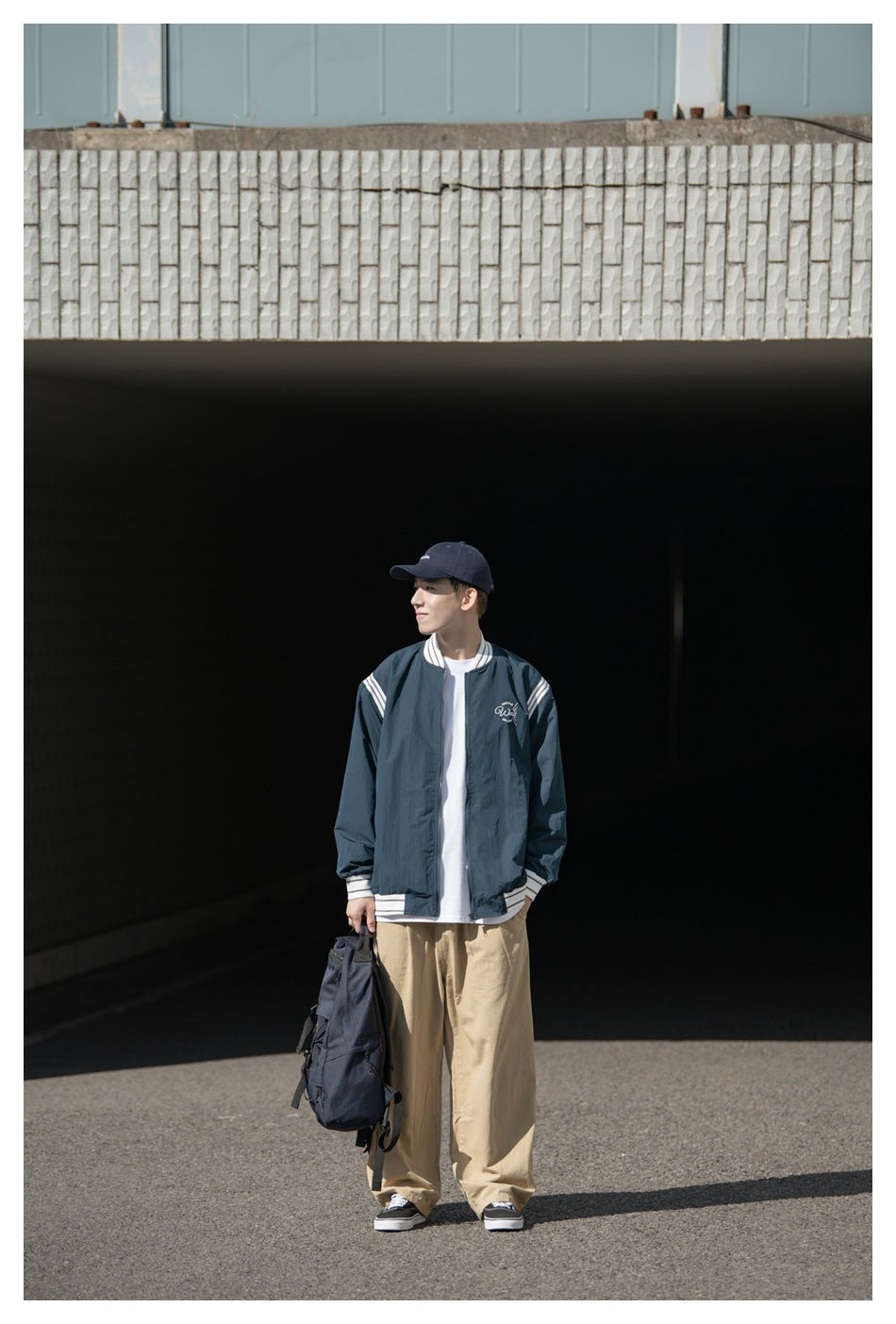 Front view of a model wearing a dark teal zip jacket with white striped trim and a small chest design.