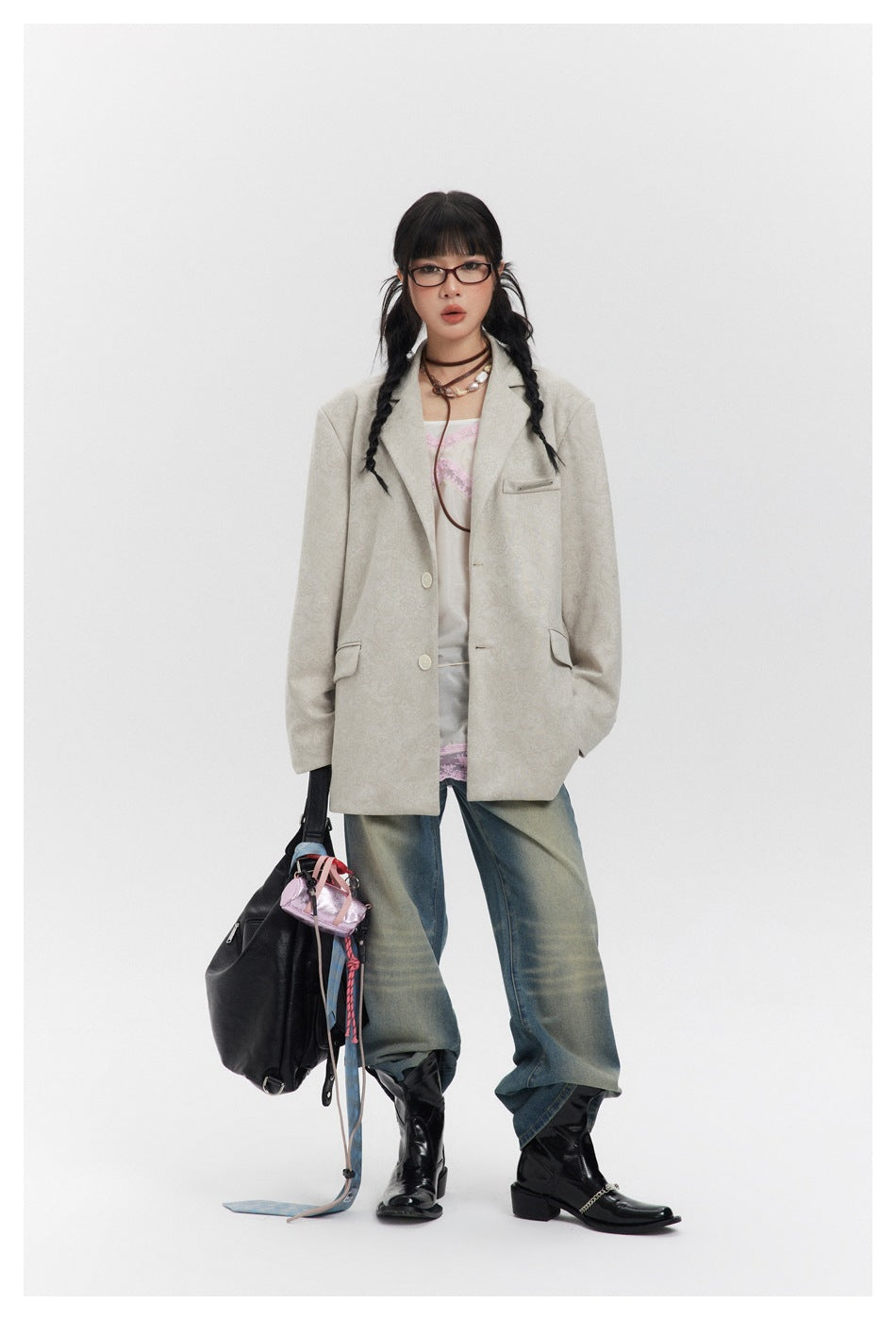 Model standing in the oversized beige patterned blazer jacket over a pink lace top with jeans and black boots