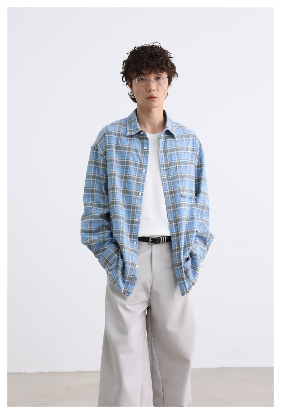 Model wearing an open blue plaid shirt over a white top, showing its frayed chest pocket and hem.