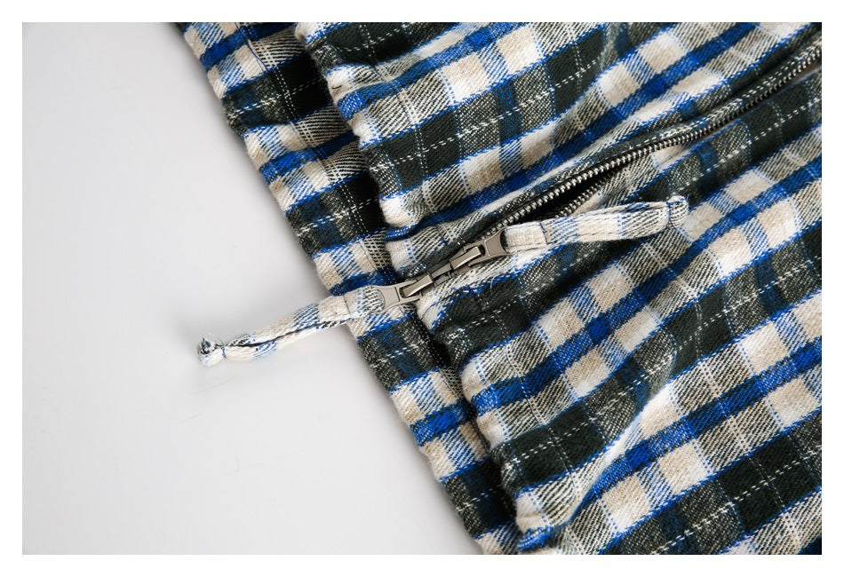 Close-up of a metal zipper and matching plaid fabric pull on blue, black, and cream checked material.