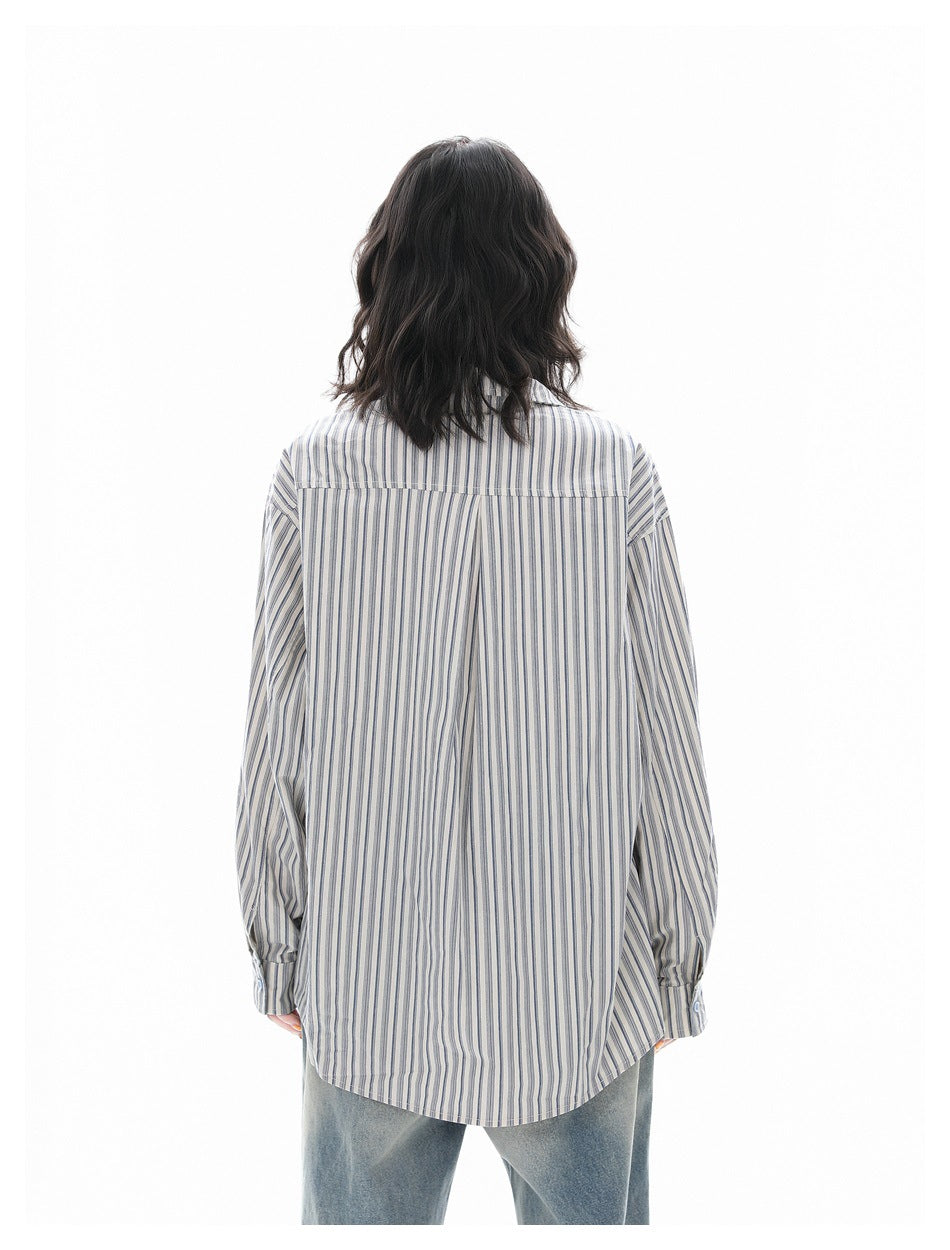 Back view of a model wearing an oversized cream shirt with narrow blue-gray vertical stripes and a curved hem.