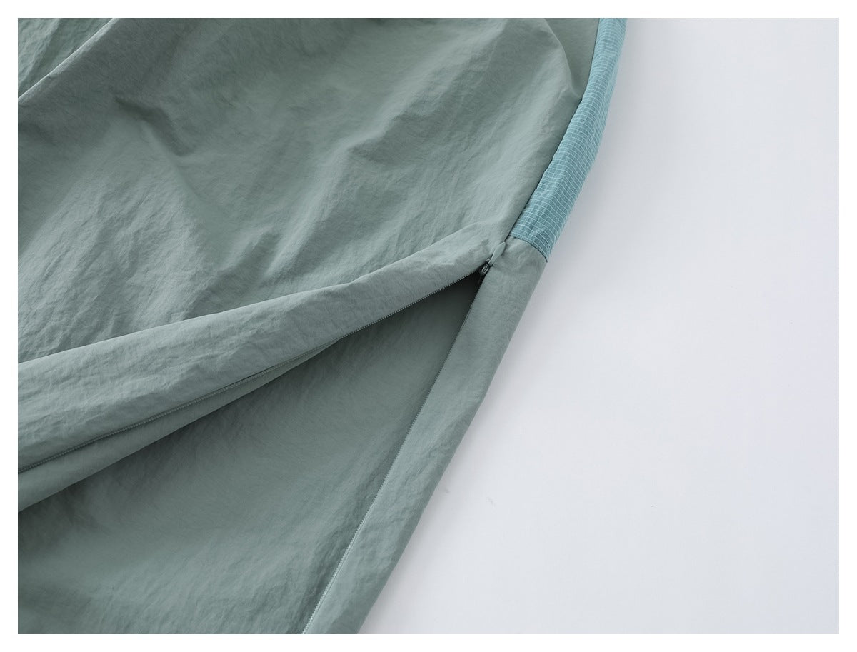 Close-up of a sage green pant leg with a side zipper and blue grid-patterned panel.