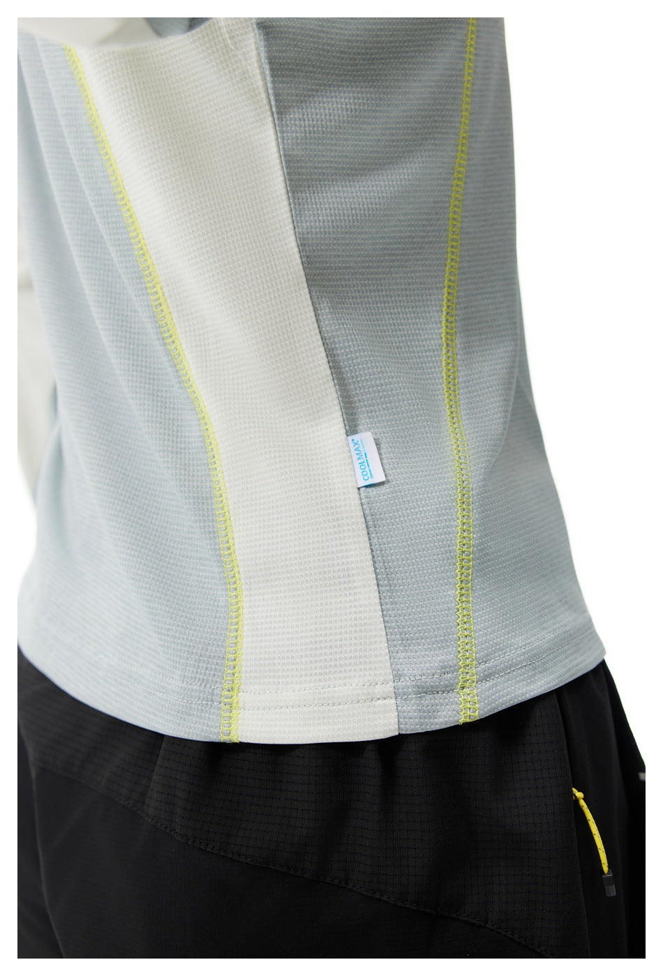 Close-up of a light gray and white athletic top with bright yellow seam stitching, worn above black shorts.