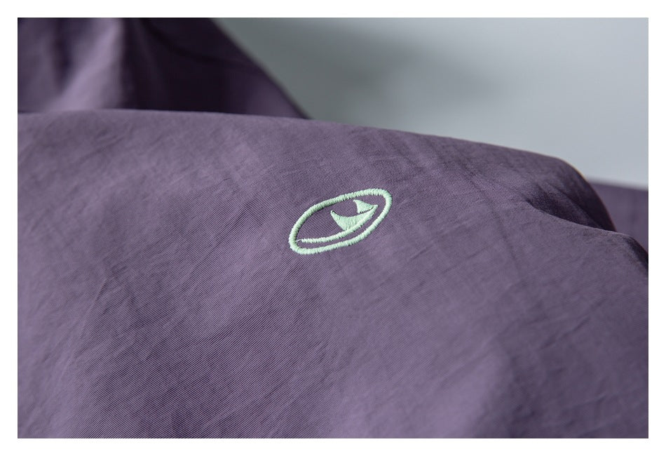 Close-up of a small pale green embroidered emblem on purple fabric.