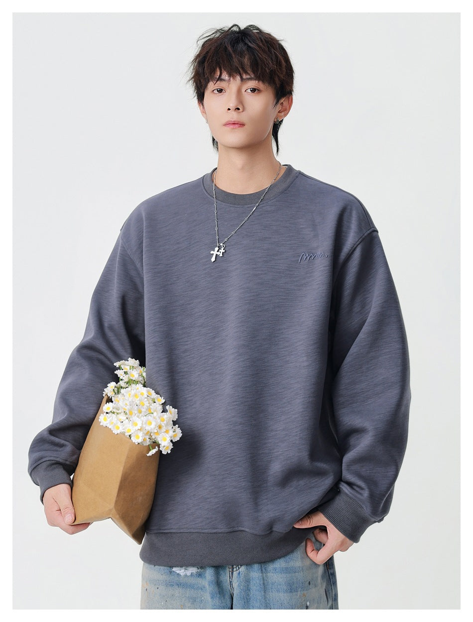 Model wearing a charcoal gray oversized crewneck sweatshirt with a small embroidered chest mark, holding a bouquet of white