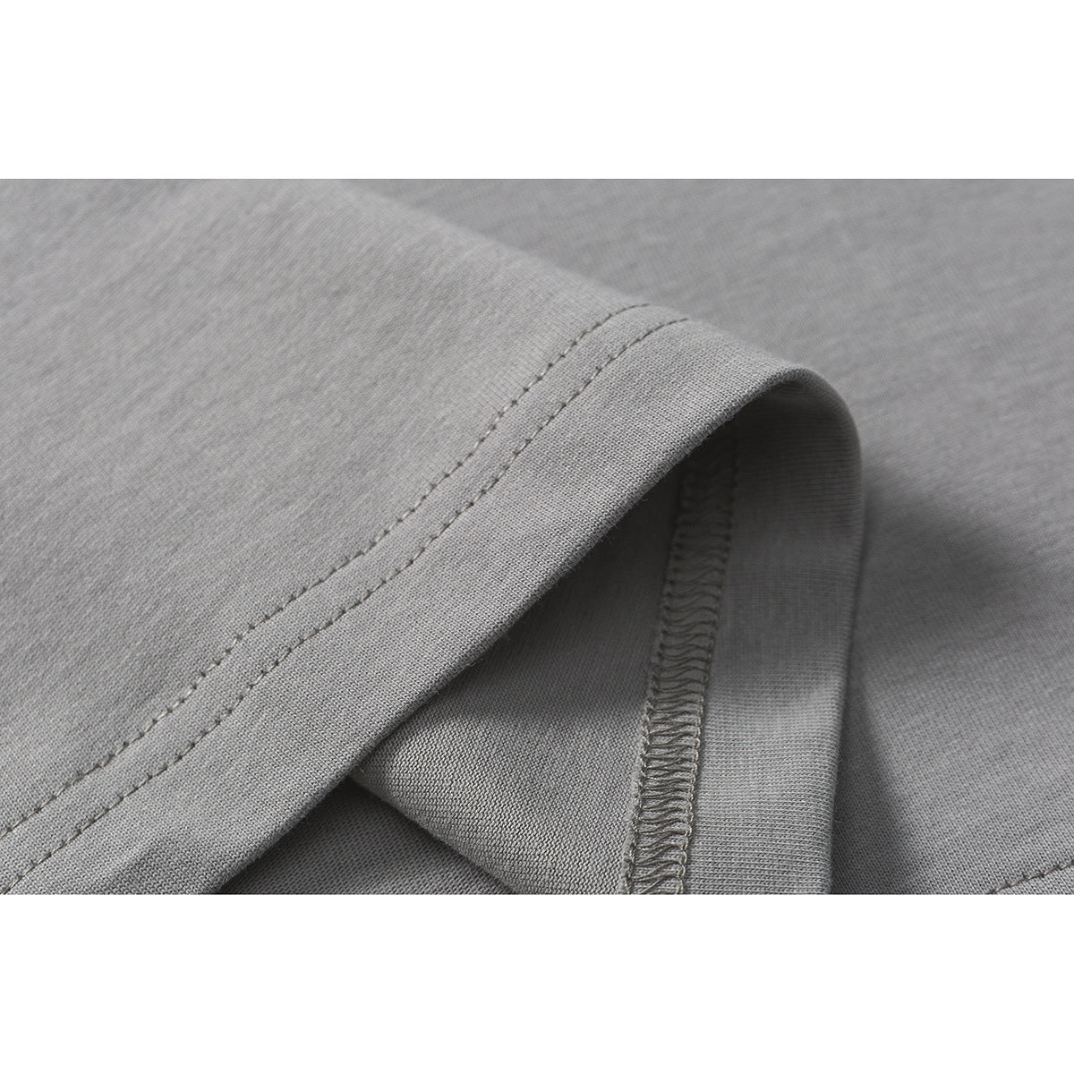 Close-up of a gray T-shirt hem showing the double-stitched edge and inner overlock seam.