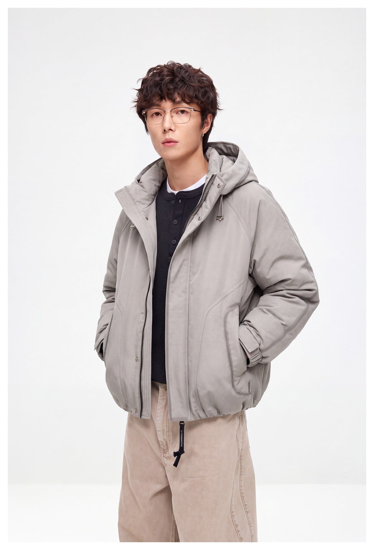 Model wearing an open light gray hooded jacket with a front zipper, snap storm flap, and angled pockets.