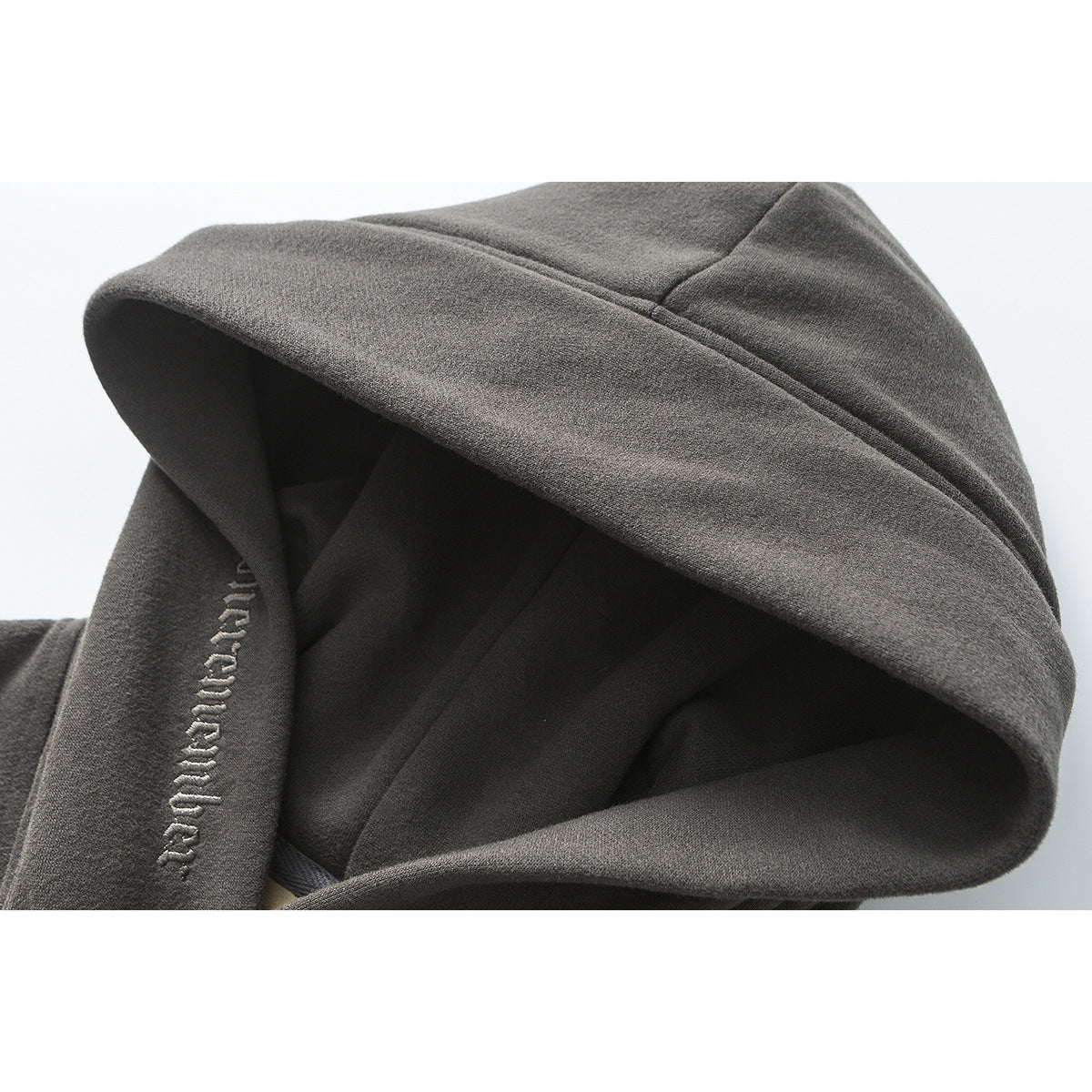 Close-up of a charcoal hoodie’s oversized hood with raised embroidered lettering along the edge.