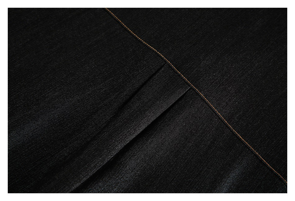 Close-up of dark black fabric with a diagonal tan-stitched seam and folded panel.