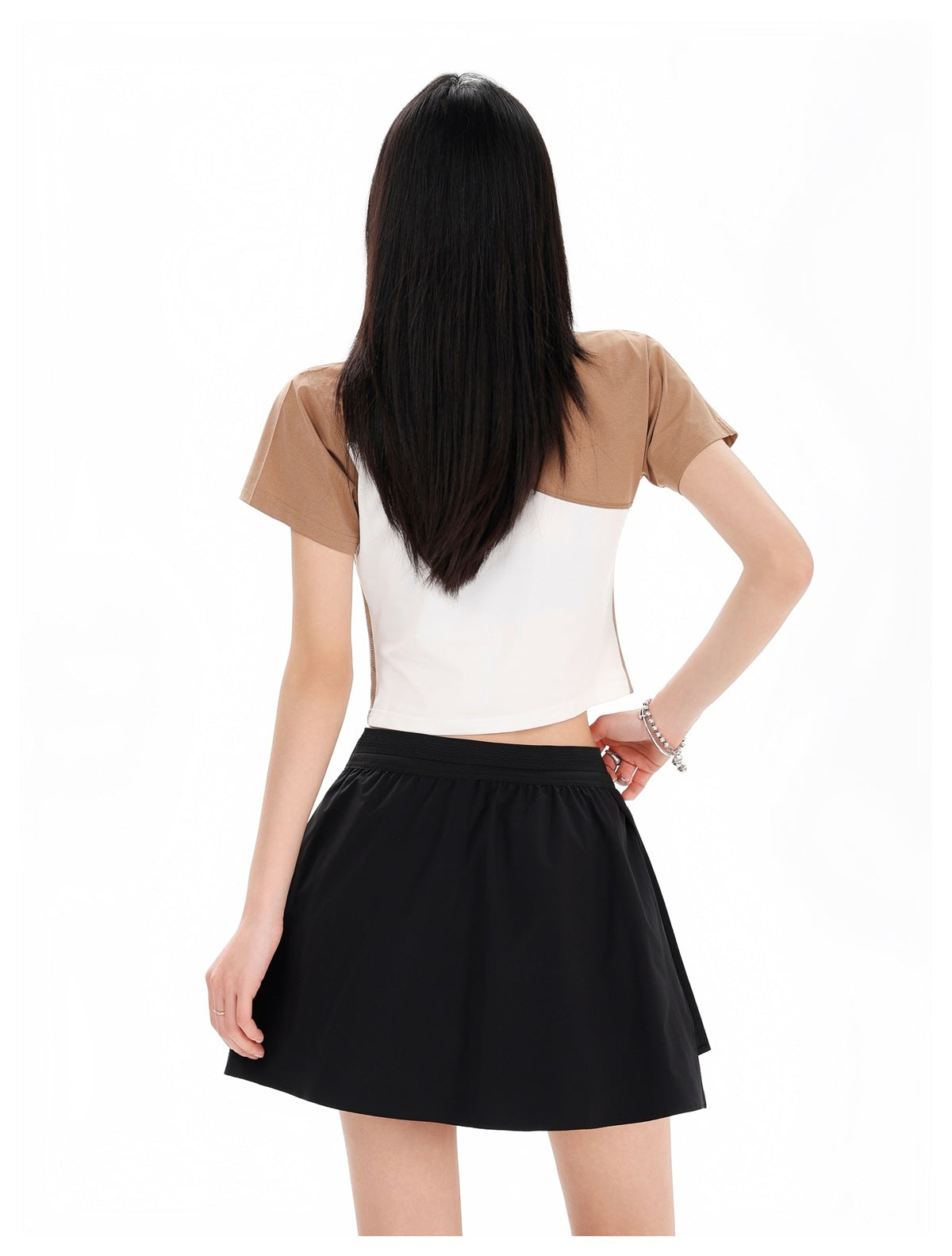 Rear view of a model wearing a brown-and-white cropped T-shirt and black flared mini skirt.