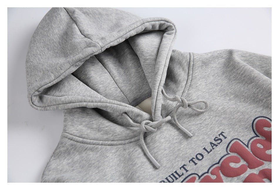 Close-up of a heather-gray hoodie showing its lined hood, drawstrings, and part of a red and navy chest graphic.