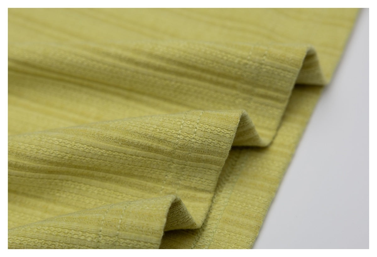 Close-up of mustard-yellow fabric folded into soft ridges, showing a subtle woven stripe texture.