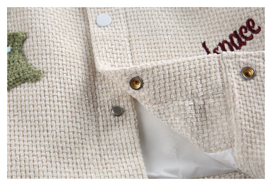 Close-up of an ivory jacket's open snap closure, showing metal fasteners, lining, and partial embroidered lettering.
